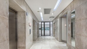 Un pasillo moderno con ascensores y puertas de vidrio, suelo de baldosas e iluminación empotrada en el techo.