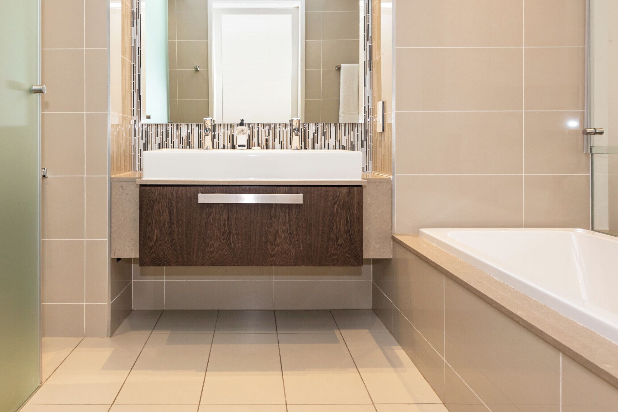 Ein modernes Badezimmer mit einer großen Badewanne, einem Waschtisch inklusive Spiegel und einem gefliesten Boden.