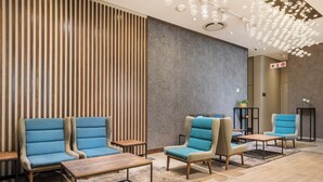 Un vestíbulo moderno con tres sillones azules, una mesa de centro de madera y un muro estampado.
