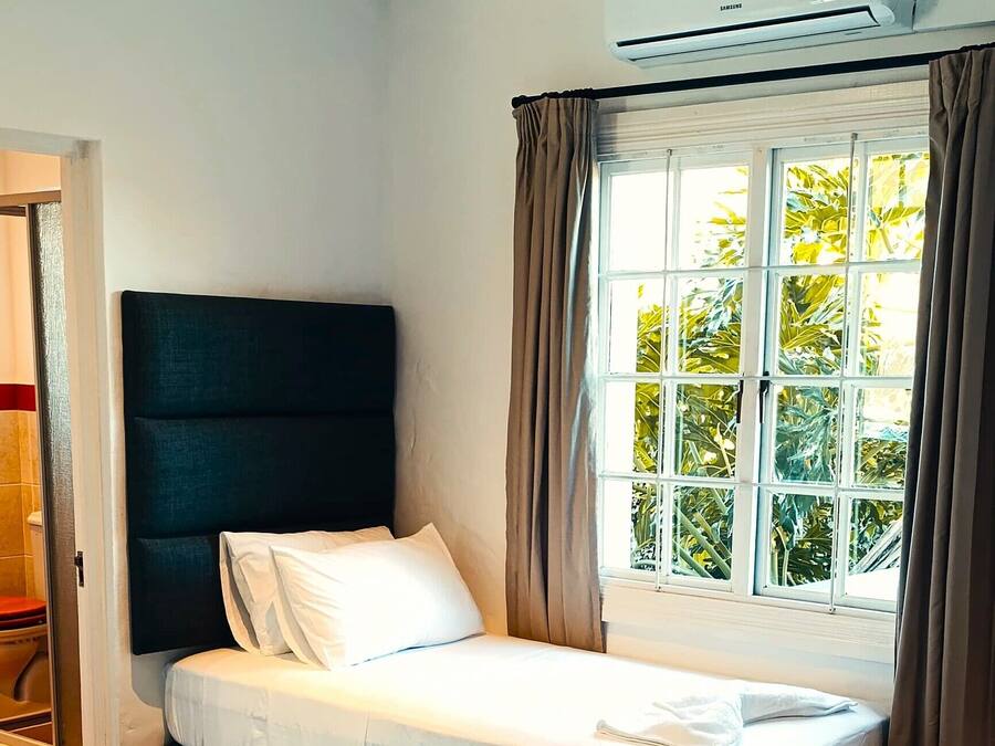 Una habitación de hotel con una cama, una ventana con cortinas, un equipo de aire acondicionado y una puerta.