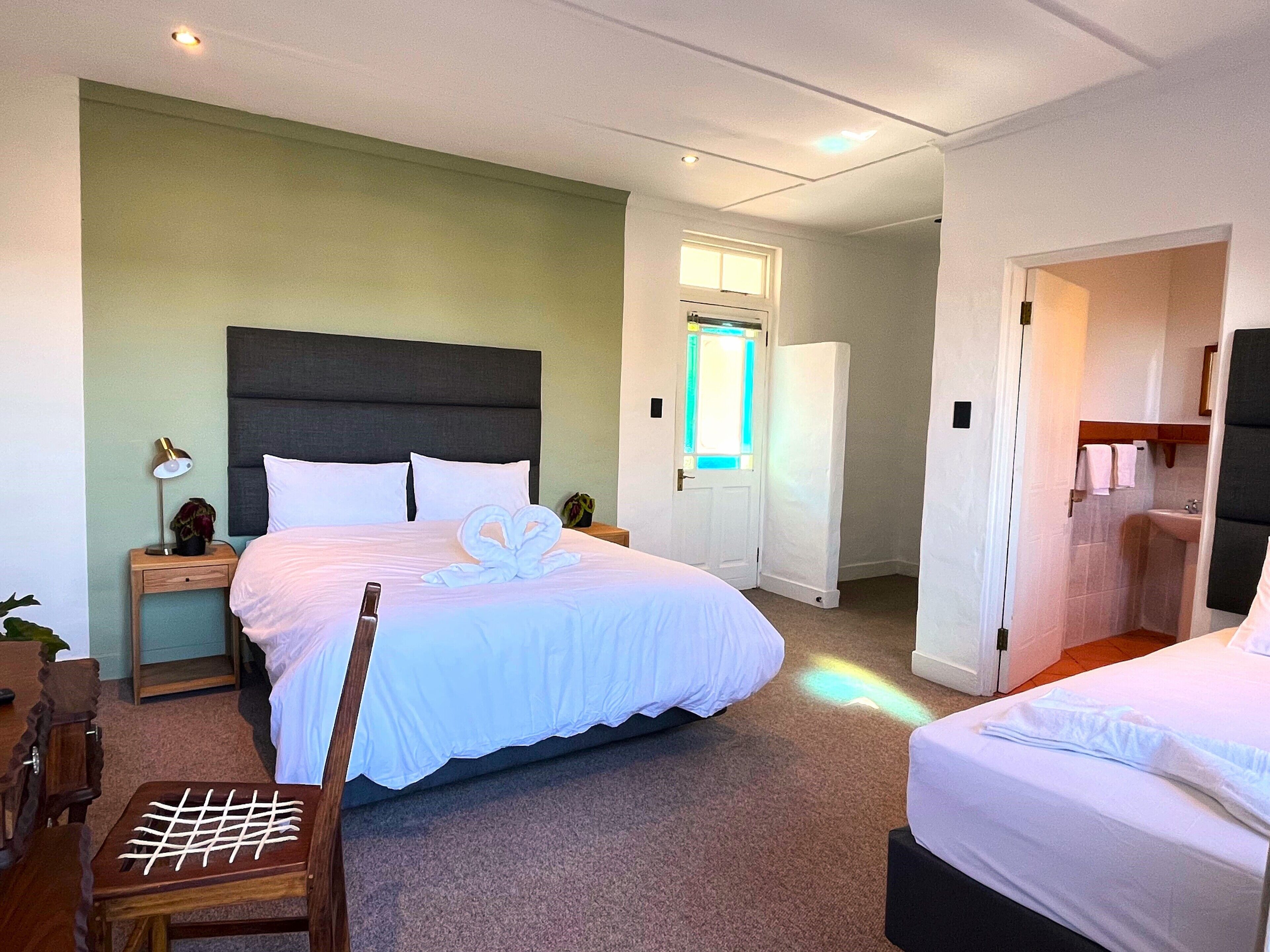 A hotel room with a large bed, a nightstand with a lamp, a wooden chair, and a small table with a white object on it.