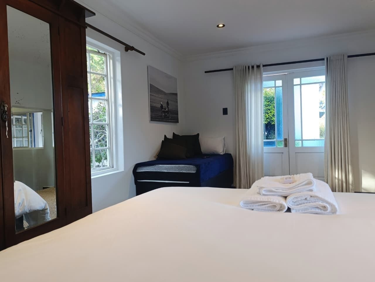 A hotel room with a large bed, a bedside table, a wardrobe, a window with curtains, and a painting on the wall.