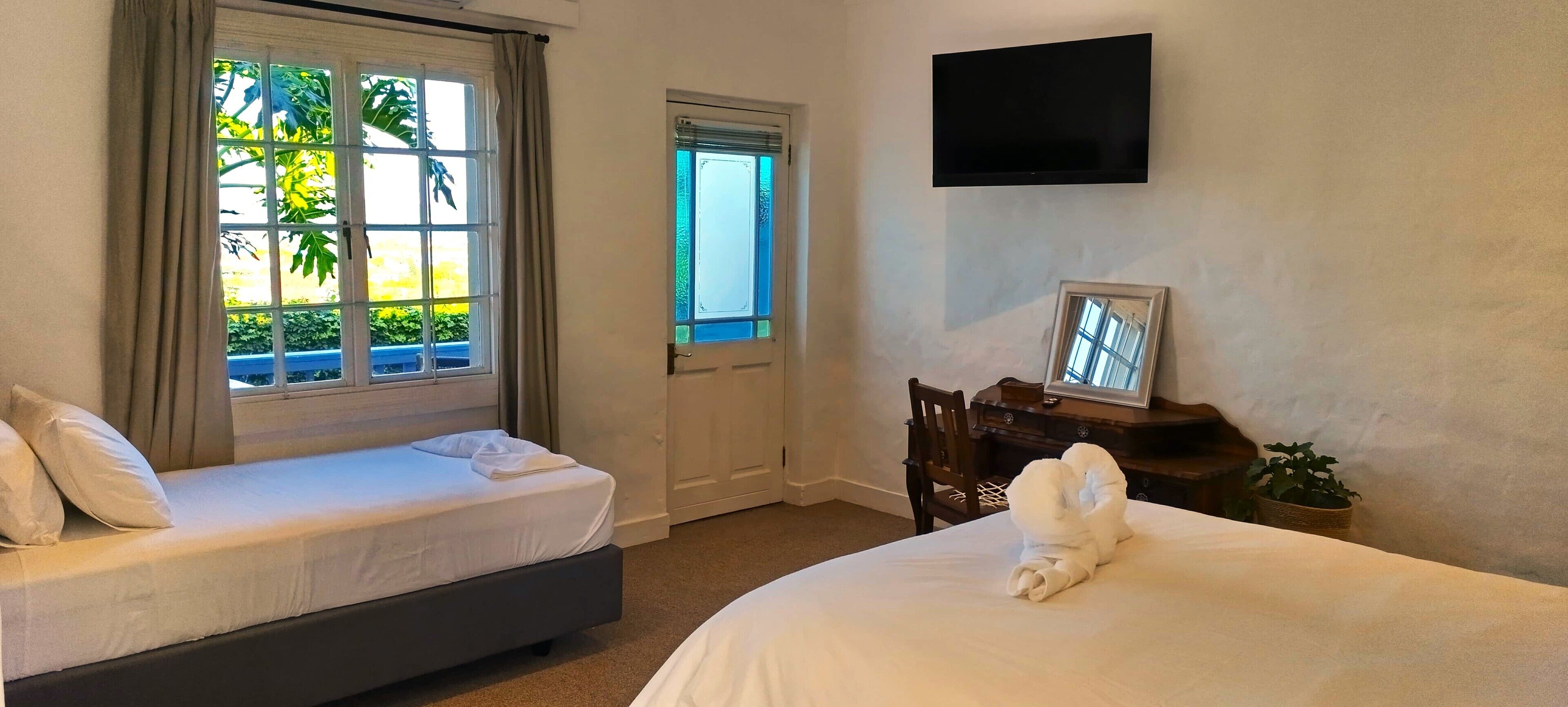 A hotel room with two beds, a TV mounted on the wall, a door, and a window with curtains.