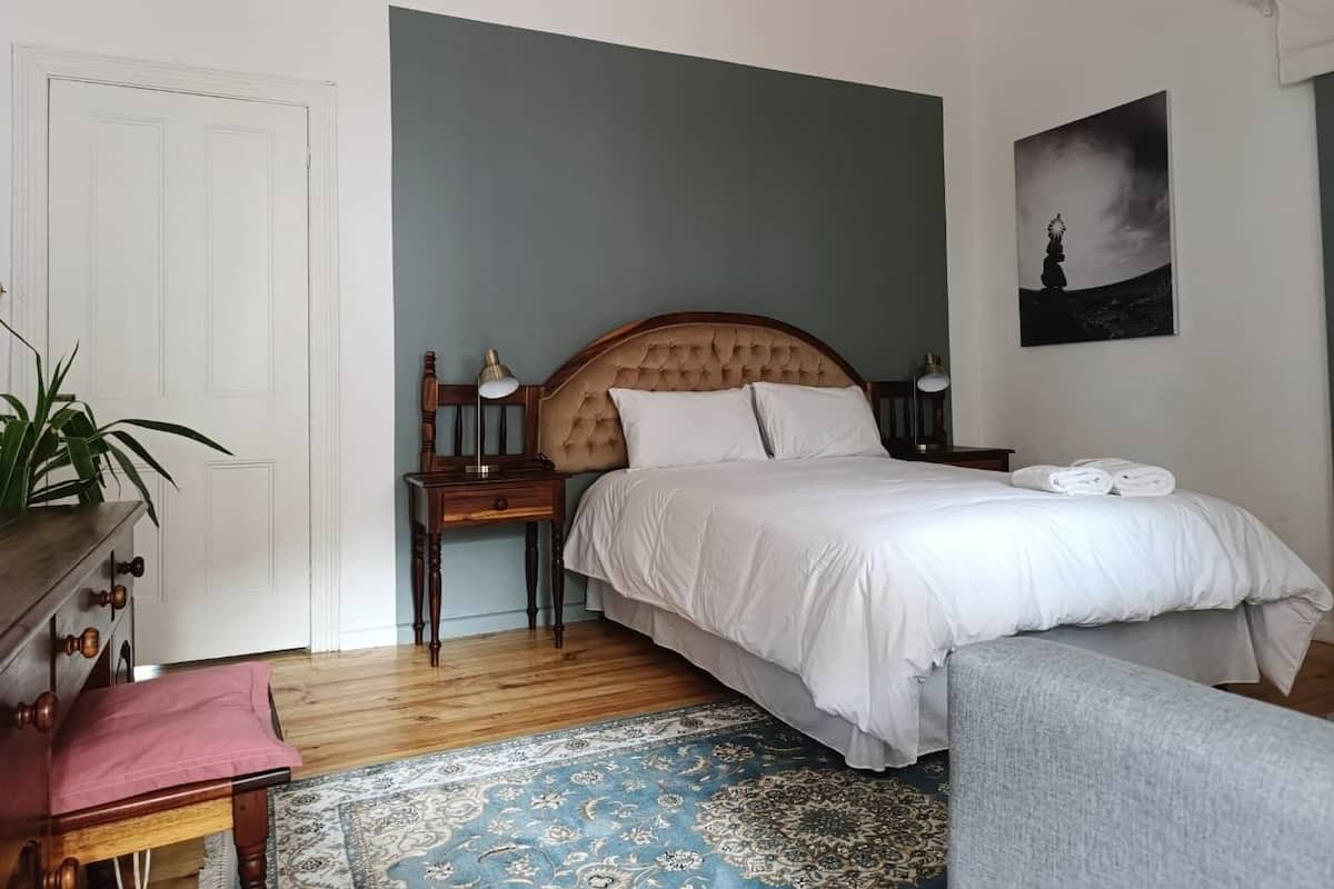 A bedroom with a bed, bedside tables, a chair, a desk, a plant, and a rug.