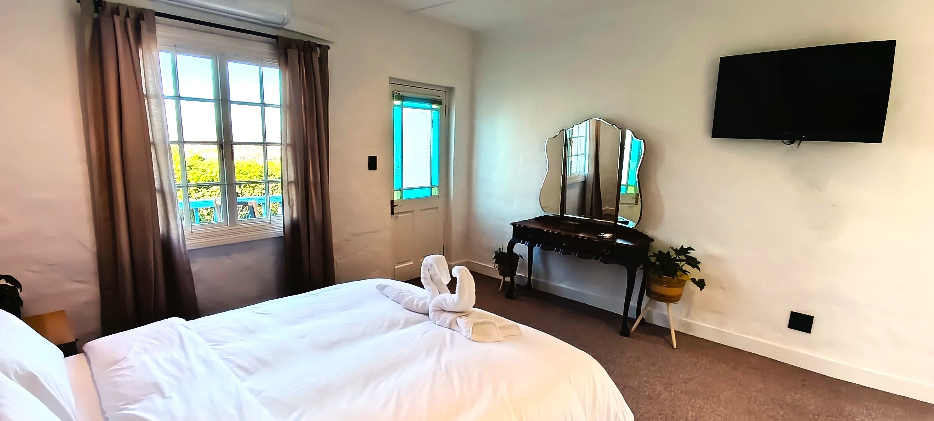 Une chambre d’hôtel avec un lit, un bureau doté d’un miroir, une télévision et une fenêtre avec des rideaux.