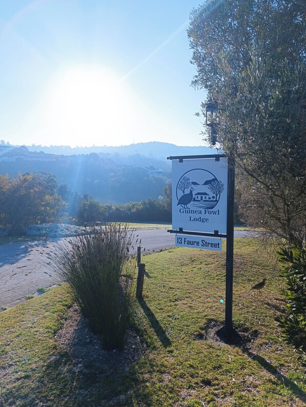 A sign for Guinea Fowl Lodge at 13 Faure Street, with a view of a river and hills in the background. - Guinea Fowl Lodge (Knysna)