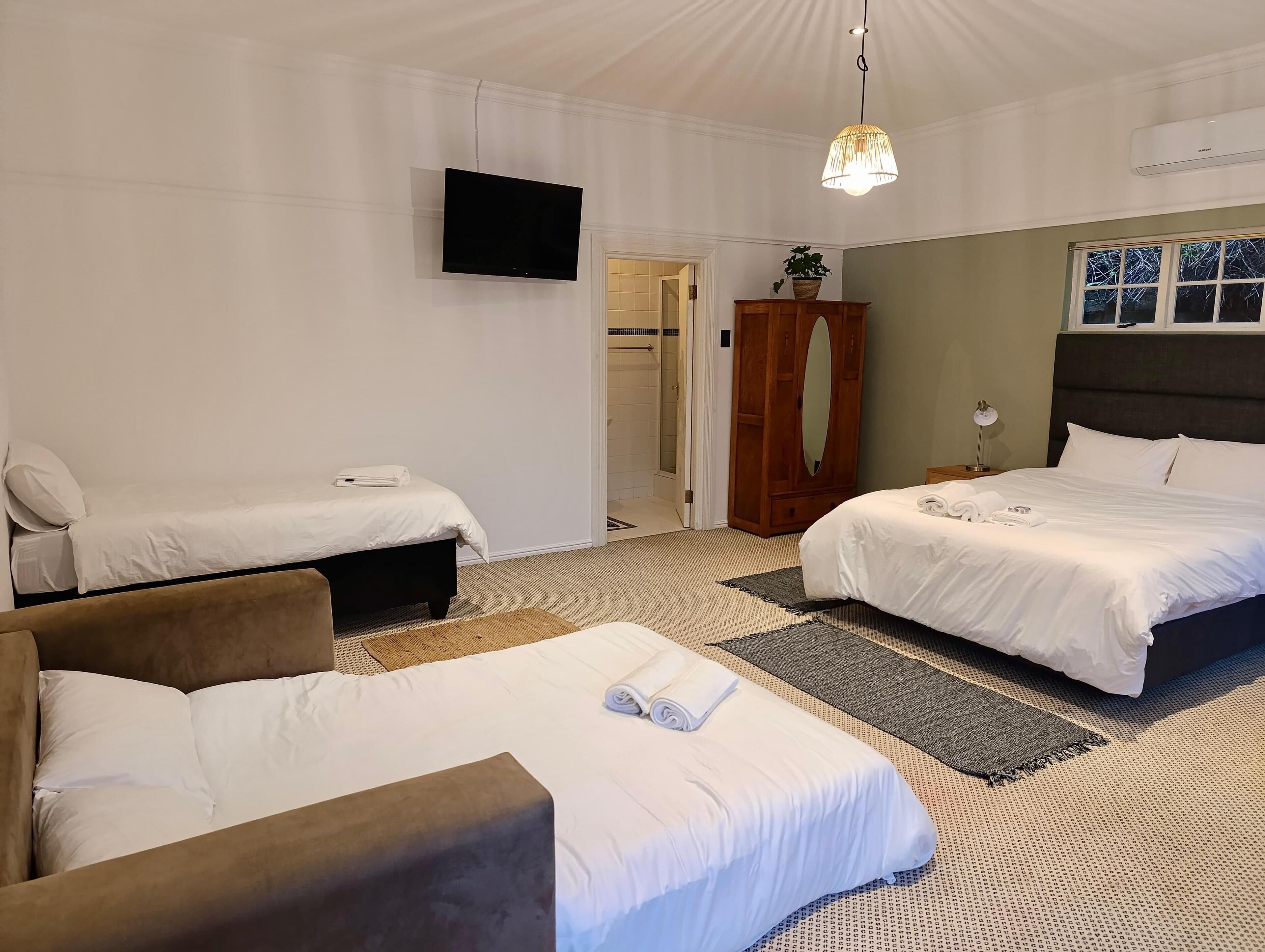 Une chambre d’hôtel avec deux lits simples, un canapé, une télévision, une armoire et une salle de bain visible à travers une porte ouverte.