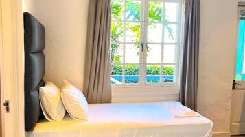 A bedroom with a bed, an air conditioning unit, a window with curtains, and a view of greenery outside.