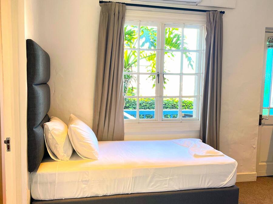 A bedroom with a bed, an air conditioning unit, a window with curtains, and a view of greenery outside.