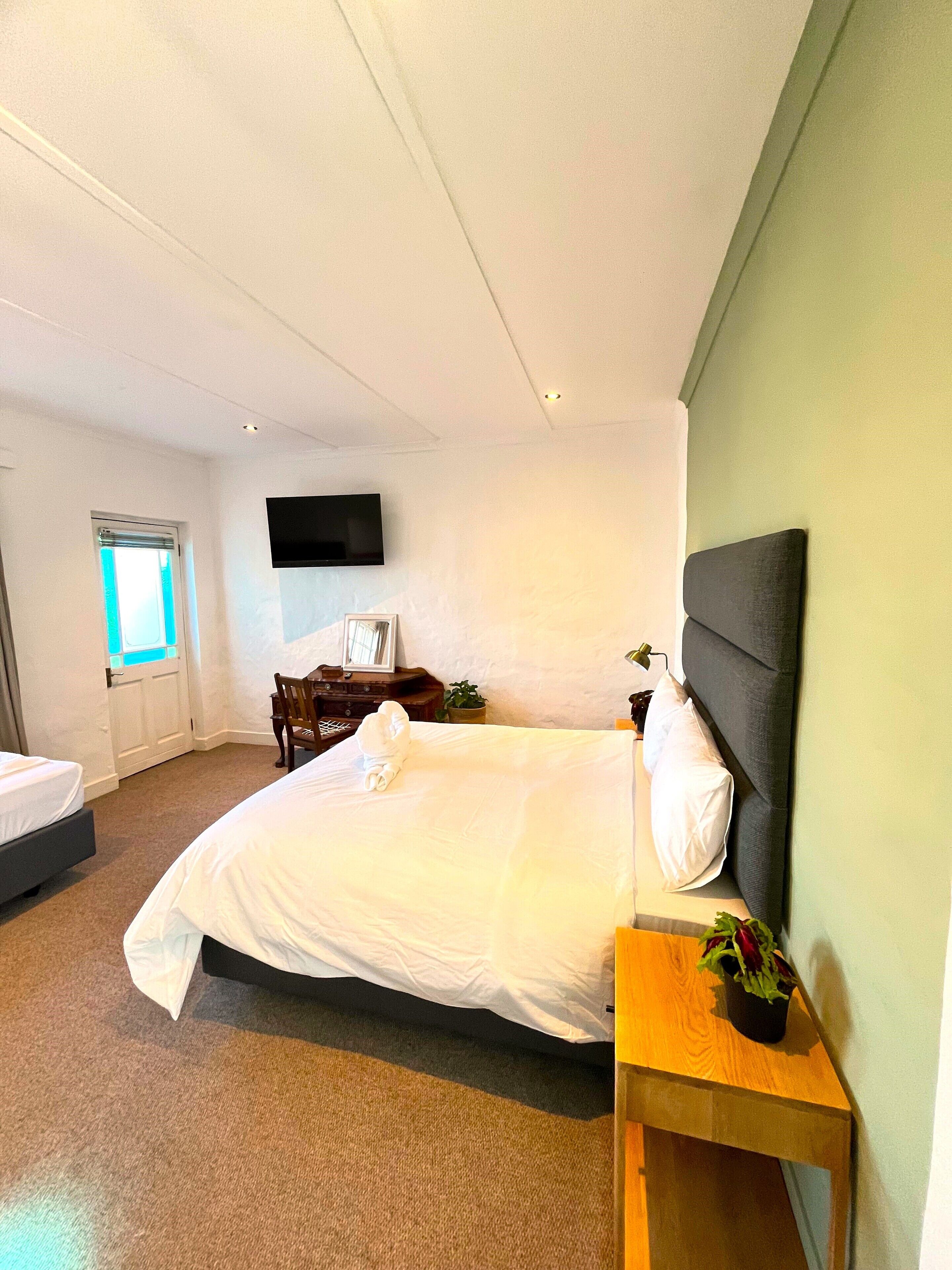 Een moderne hotelkamer met een groot bed, een houten nachtkastje, een flatscreen-tv aan de muur en een klein raam met uitzicht.