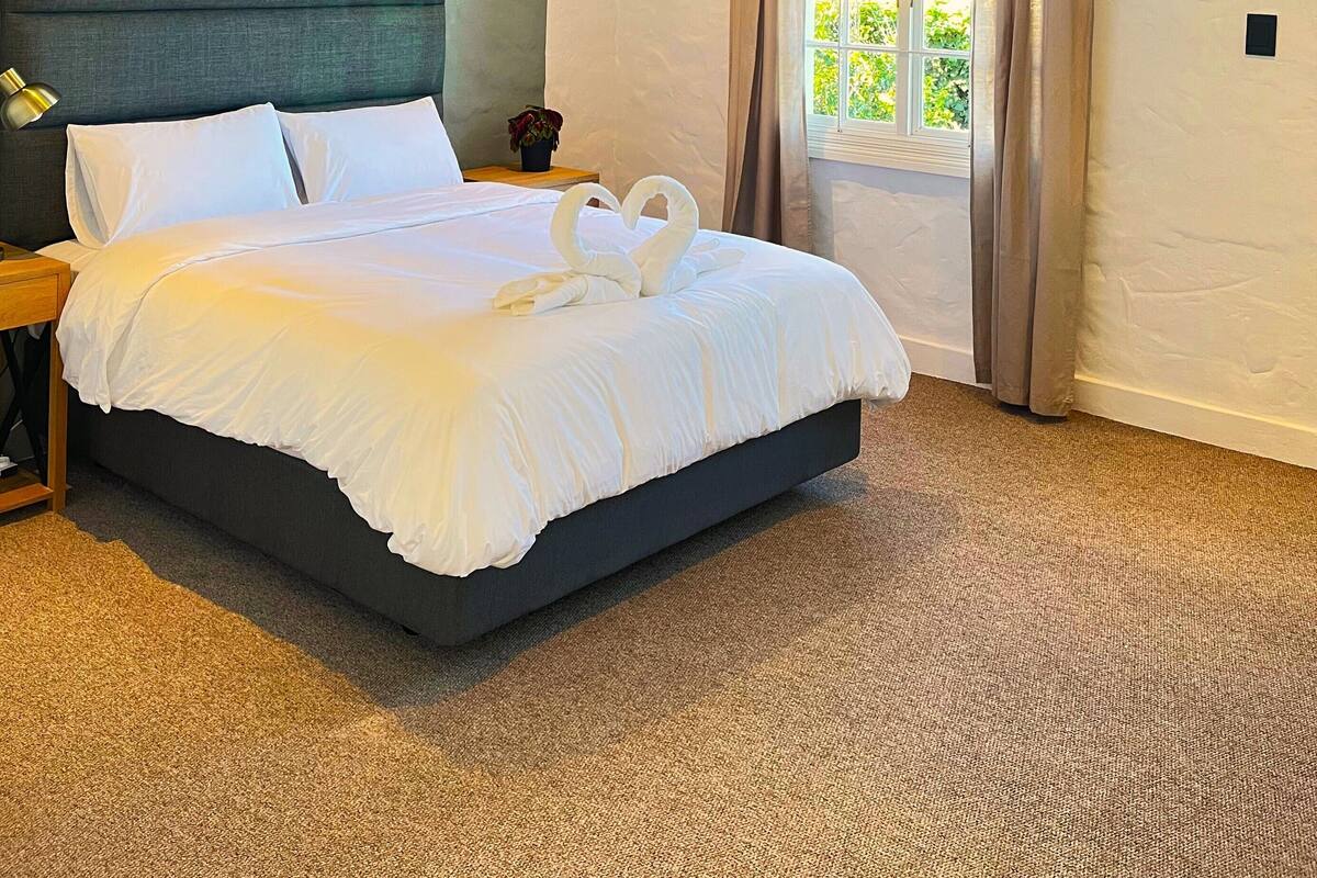 A hotel room with a large bed, a headboard, a nightstand, a lamp, a window with curtains, and an air conditioning unit.