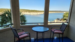 Ein Balkon mit zwei Stühlen und einem Tisch, mit Blick auf einen Strand und einen Poolbereich.