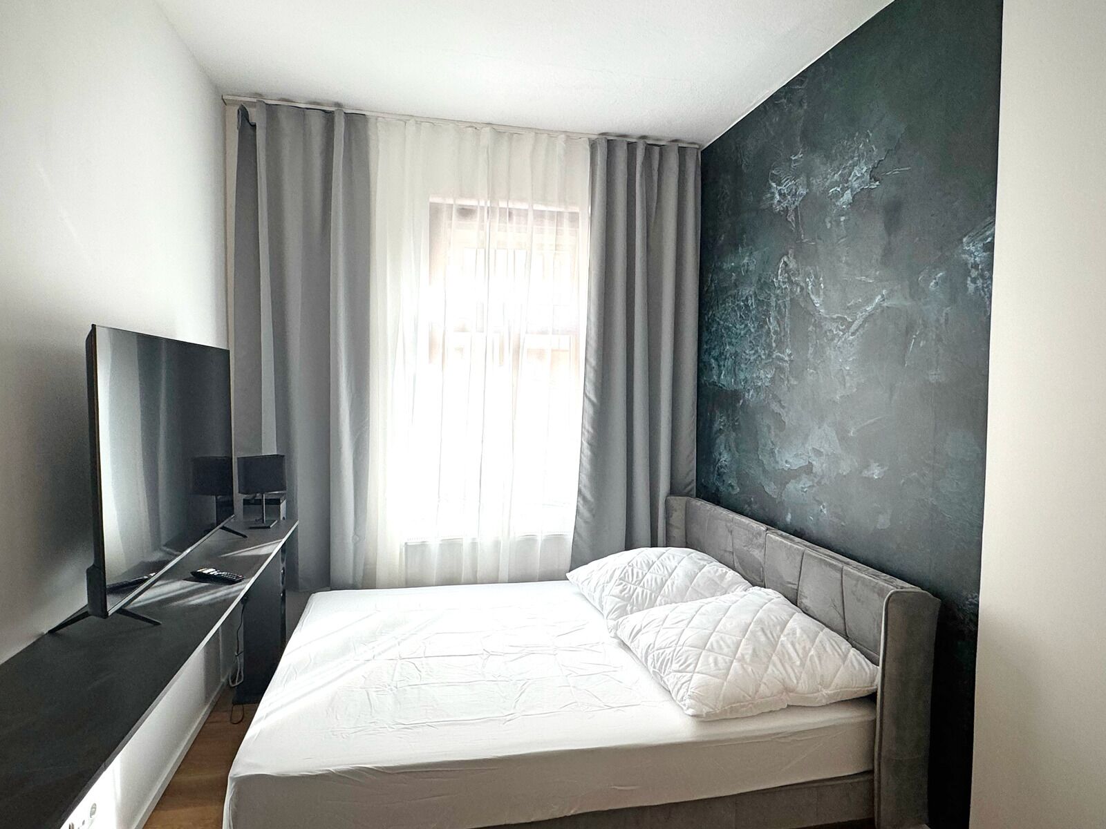 Ein modernes Hotelzimmer mit einem Bett, einem Flachbildfernseher, einem Schreibtisch und einem großen Fenster mit Vorhängen.