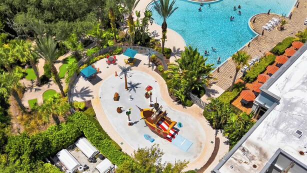 Vista aérea de un resort con una piscina grande, palmeras y una atracción con forma de barco pirata.