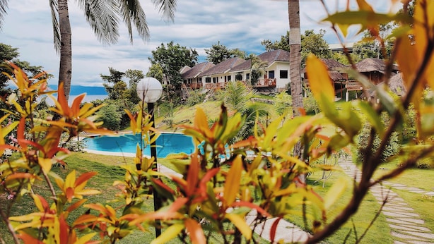 Un resort con piscina, palmeras y edificios de techo de paja.