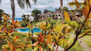 A resort with a swimming pool, palm trees, and thatched-roof buildings.