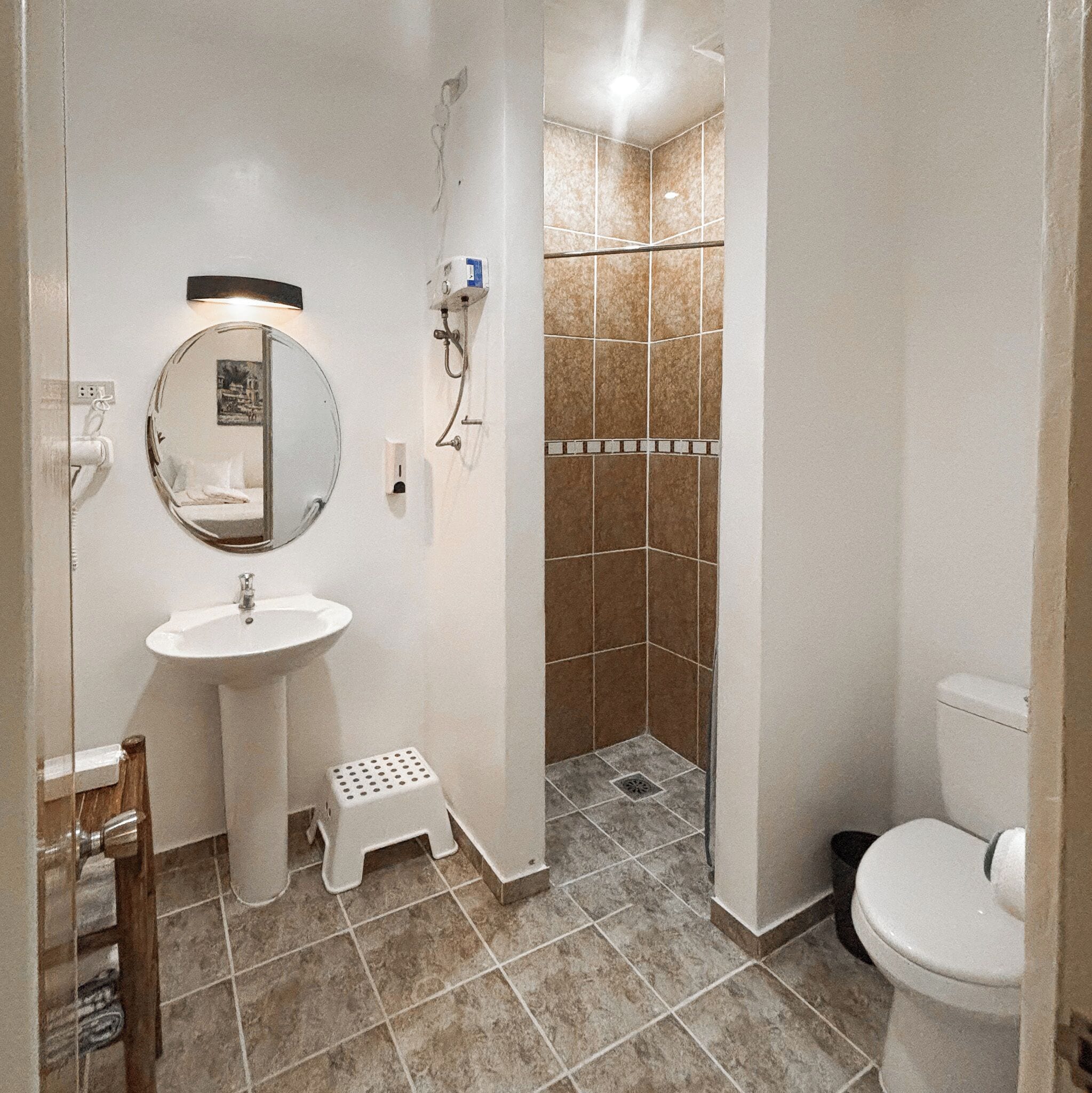 Un baño con lavamanos pedestal, espejo, inodoro y zona de ducha.