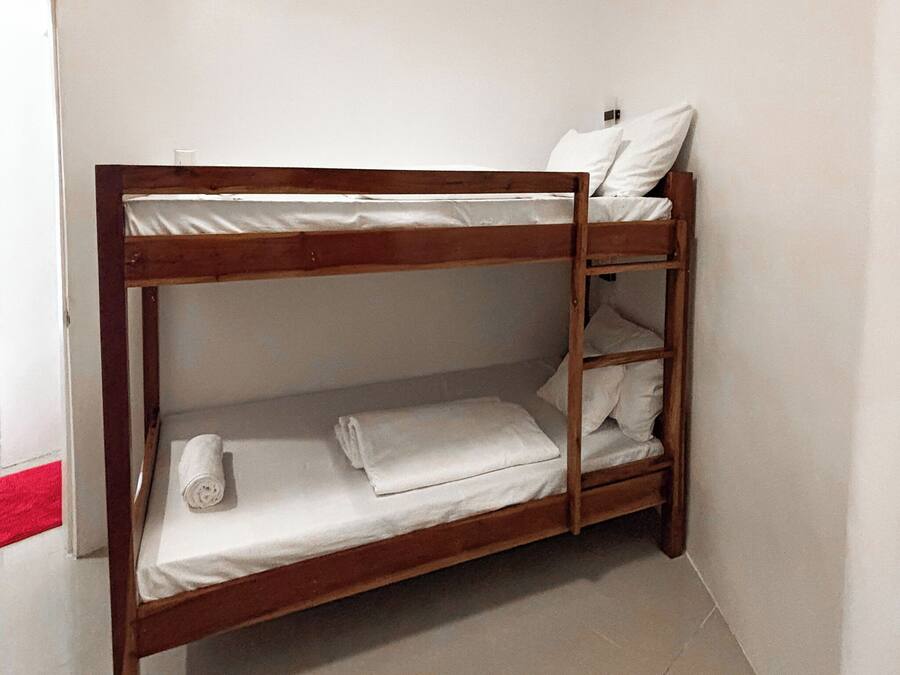 Ein Stockbett mit weißer Bettwäsche und Kissen, ein Holzrahmen und ein roter Teppich im Flur.