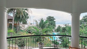 Un balcón con vista a una piscina, palmeras y una playa distante.