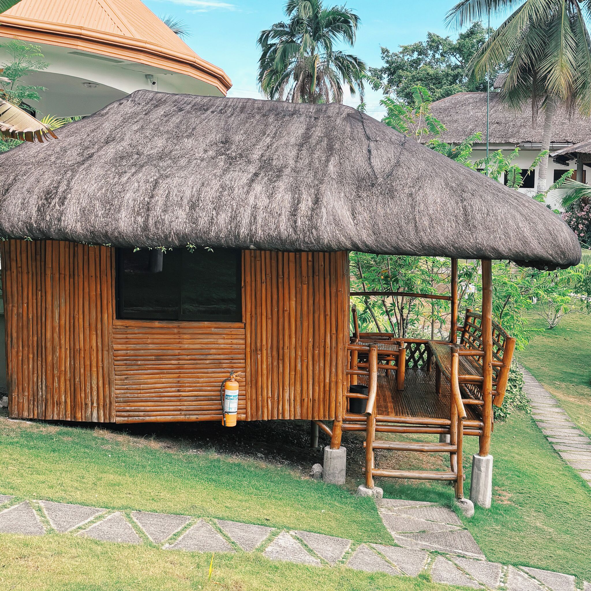 A small wooden hut with a thatched roof, a fire extinguisher mounted on the wall, and a wooden bench outside.