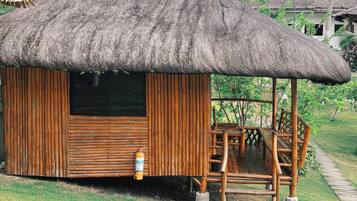 A small wooden hut with a thatched roof, a fire extinguisher mounted on the wall, and a wooden bench outside.