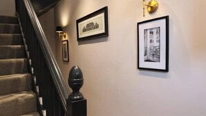 A staircase with a black balustrade, a wall-mounted lamp, and two framed pictures.