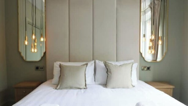 A hotel room with a large bed, two bedside tables, and two wall-mounted mirrors.