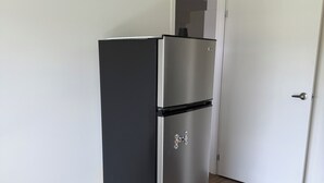 A compact kitchen with a black and silver refrigerator, a white door, and wooden flooring.
