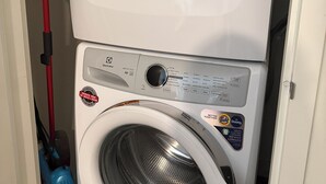A stacked washer and dryer unit with a control panel, a red mop, and a blue cleaning tool.