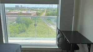 A room with a large window, a bed, a desk, and a chair.