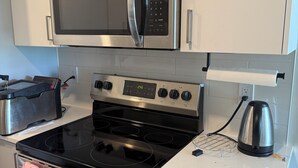 A kitchen with stainless steel appliances, including a microwave, oven, and stove. There are cabinets above the stove and a kettle on the countertop.