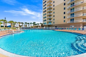A swimming pool with lounge chairs, a tall building with balconies, and palm trees.