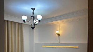 En pænt redt seng med hvide sengetøj og et beige tæppe, en vægmonteret lysarmatur og et natbord med en lampe.