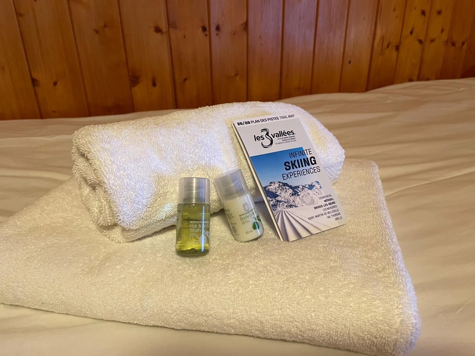A neatly folded white towel on a bed with a brochure and two toiletry bottles.
