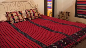 Un lit avec une couvre-lit à rayures rouges et noires, des oreillers blancs et une tête de lit en bois.