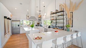 A modern kitchen with white cabinetry, a central island, and a dining area with white chairs. - Farmstay Estate | Pool & Honey Farm | Cedar Hot Tub | Healdsburg | Sleeps 8 (Healdsburg)