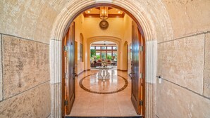 A grand entrance with a circular marble floor, a central chandelier, and a view into a well-furnished lobby area.