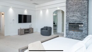 A modern bedroom with a large bed, a stone accent wall, a fireplace, a flat-screen TV, and a ceiling fan. - 4400 SqFt Luxury Estate W/Pool&Spa, Billiards, Entertainment and Comfort (Lake Havasu City)