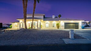 A two-story house with a garage, palm trees, and a well-lit driveway at dusk. - 4400 SqFt Luxury Estate W/Pool&Spa, Billiards, Entertainment and Comfort (Lake Havasu City)