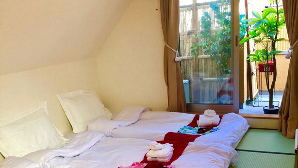 A hotel room with a large bed, a window with a view of greenery, and a hanging light fixture. - Shinjuku 120 sq.m. house / 3 min walk from JR Shin-Okubo station / 2 bathrooms, 2 toilets, parking / 10 min walk from Kabukicho (新宿区百人町)