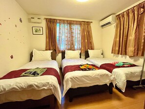 Une chambre d’hôtel avec trois lits simples, une fenêtre avec des rideaux, un appareil de climatisation et un tableau encadré au mur.