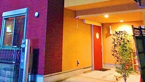 A two-story building with a red brick facade and a yellow upper section. There is a small entrance with a door and a potted plant outside. - Shinjuku 120 sq.m. house / 3 min walk from JR Shin-Okubo station / 2 bathrooms, 2 toilets, parking / 10 min walk from Kabukicho (新宿区百人町)