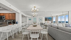 Una cocina moderna con armarios blancos, un comedor con sillas blancas y un ventanal con vistas al océano.