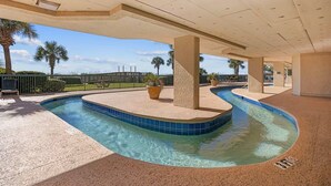 Una piscina de diseño curvo, rodeada por una zona de arena y palmeras.
