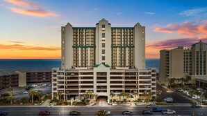 Un hotel de varios pisos con un atrium central, estacionamiento subterráneo y vista al océano al atardecer.