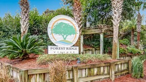 Letrero de Forest Ridge Village, con un pérgola de madera y diversas plantas.