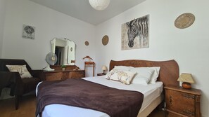 A bedroom with a bed, a chair, a dresser, a mirror, and wall art. - The Emerillon route (Royan)