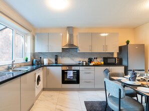 A modern kitchen with a built-in oven, a washing machine, and a dining area set for four.