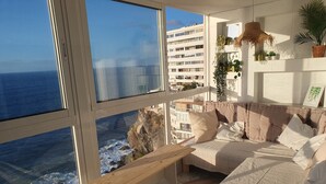 Un balcone con vista sull'oceano e su un edificio, un'area salotto con cuscini e una pianta pensile.