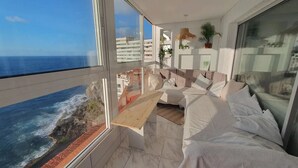Un balcone con vista sull'oceano, un divano bianco e una pianta pensile.